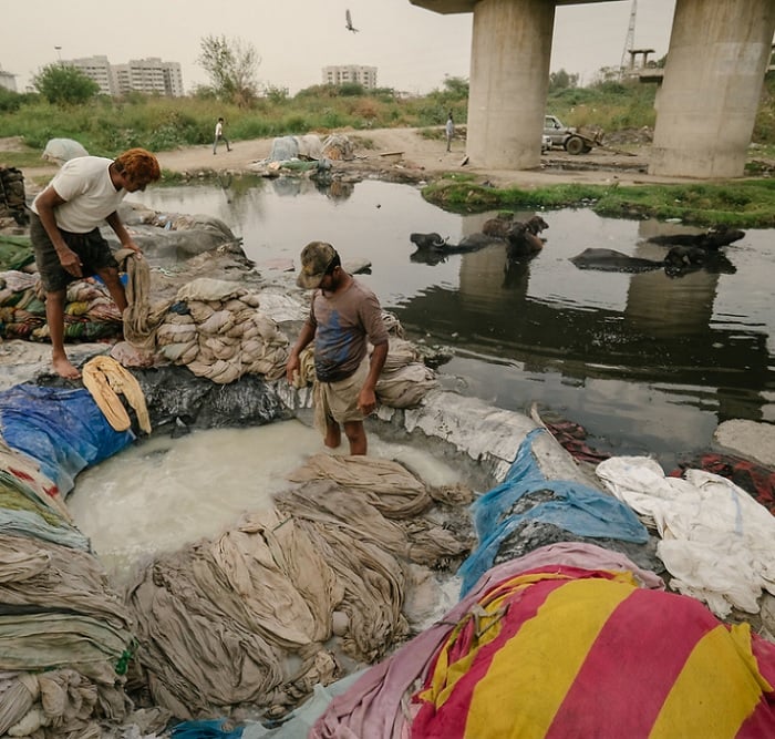 Two men washing clothes under a bridge