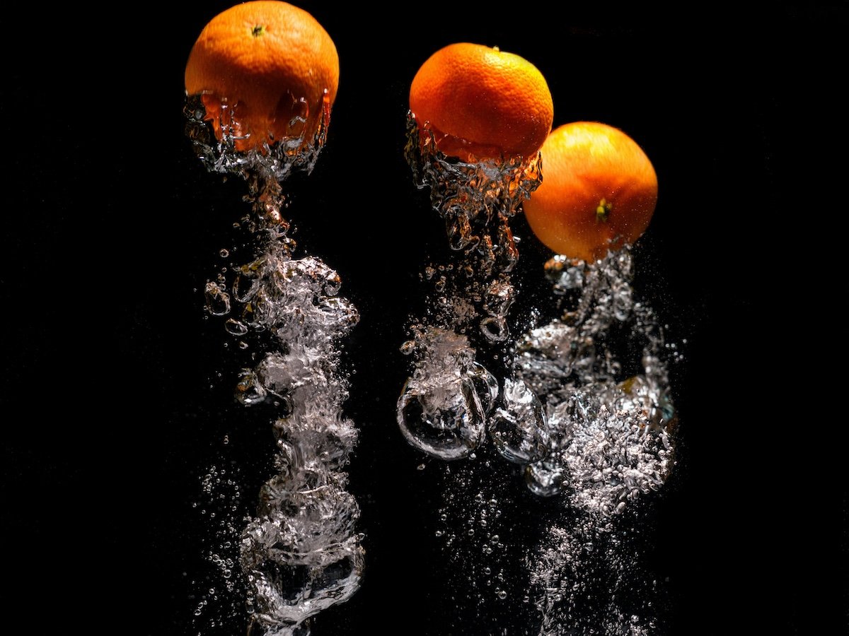 An inverted photo of oranges falling into water for high-speed photography