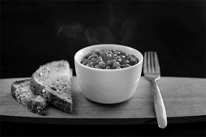 A black and white food photography shot of baked beans and bread on a wooden tray
