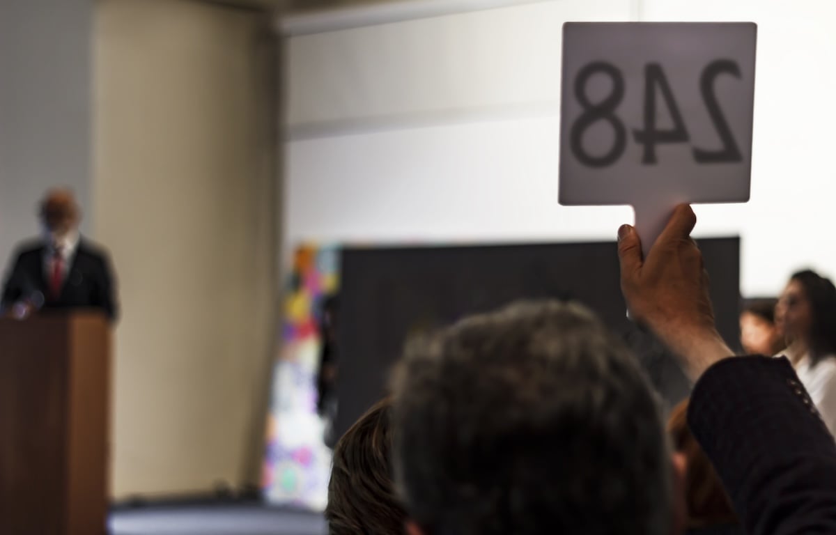 An auctioneer with a raised hand with a number on a sign to buy the most expensive photographs