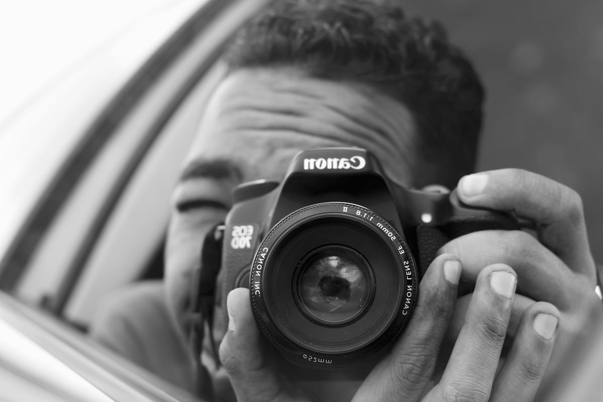 Black-and-white image of a person taking a selfie in a car mirror with a nifty fifty lens